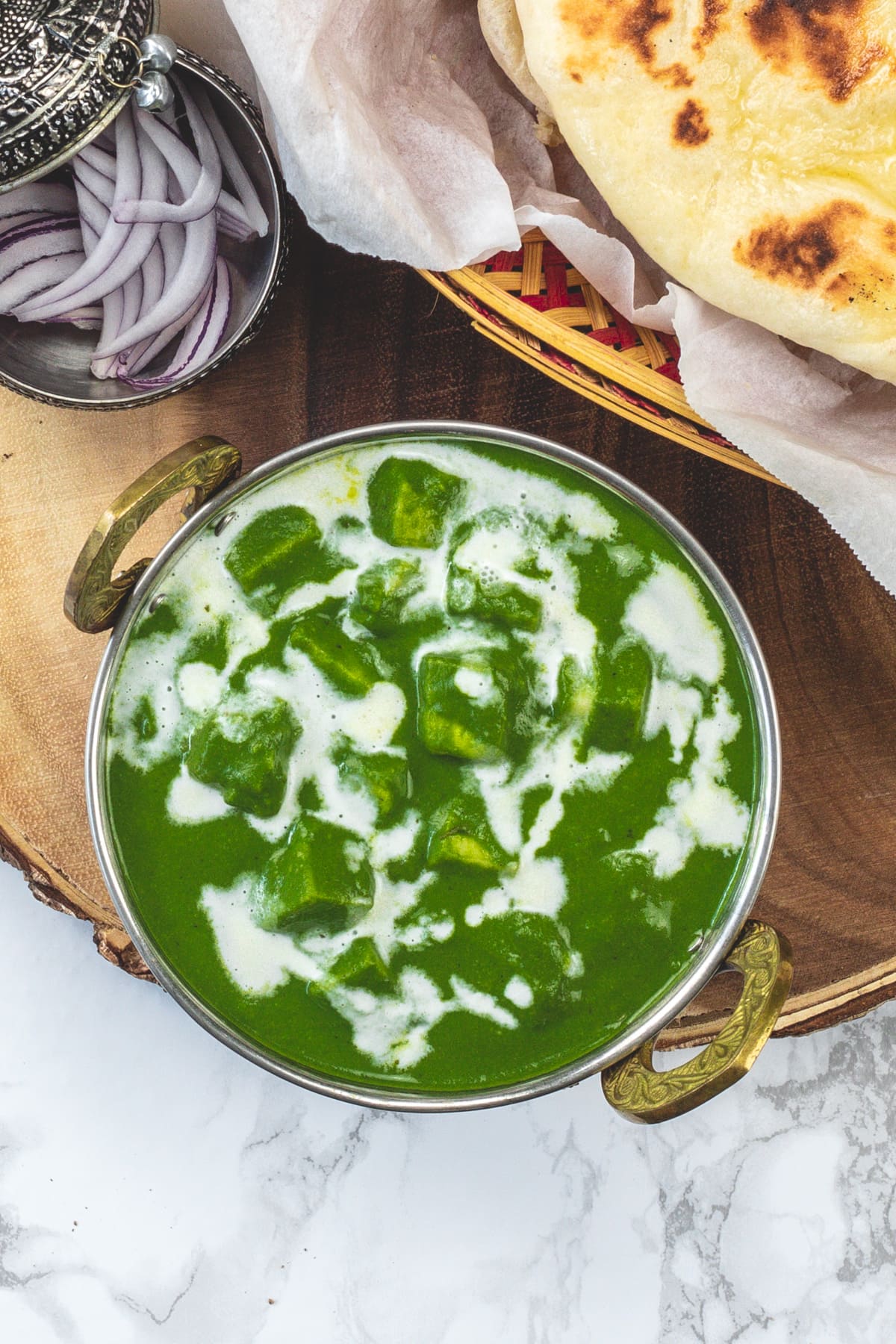 Top view of palak paneer garnished with cream, served with naan and onions.