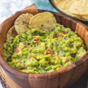 Side view of spicy guacamole with 2 tortilla chips in the bowl and more on the side.