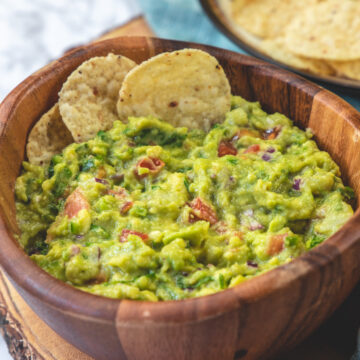 Side view of spicy guacamole with 2 tortilla chips in the bowl and more on the side.