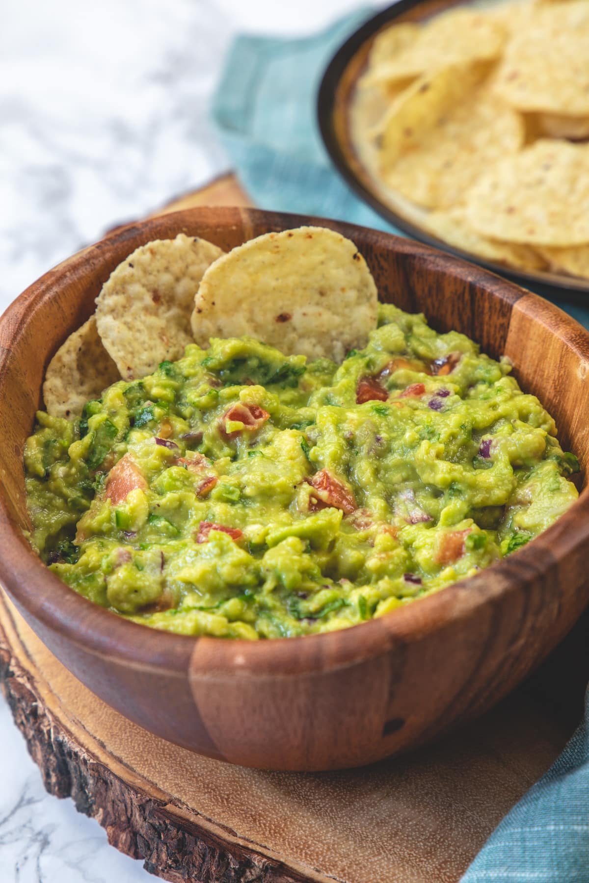 Side view of spicy guacamole with 2 tortilla chips in the bowl and more on the side.