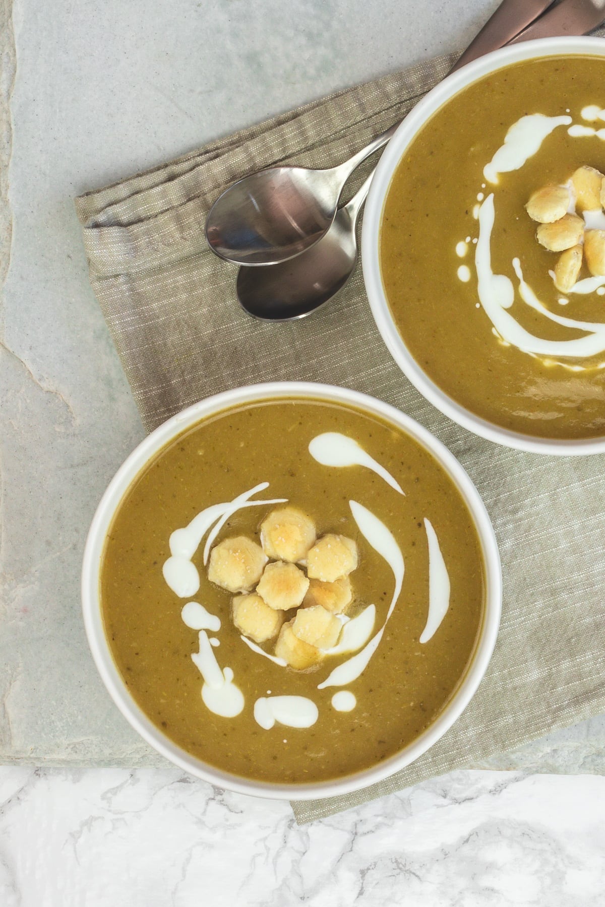 Two bowls of broccoli potato soup garnished with crackers and yogurt.