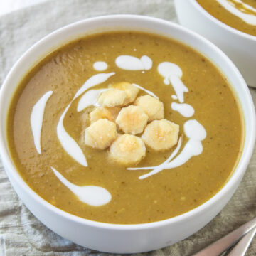 Close up of broccoli potato soup bowl with crackers and swirls of yogurt with spoons on side.