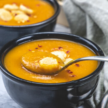 a spoonful of carrot tomato soup is taken from the bowl and another bowl in the back.