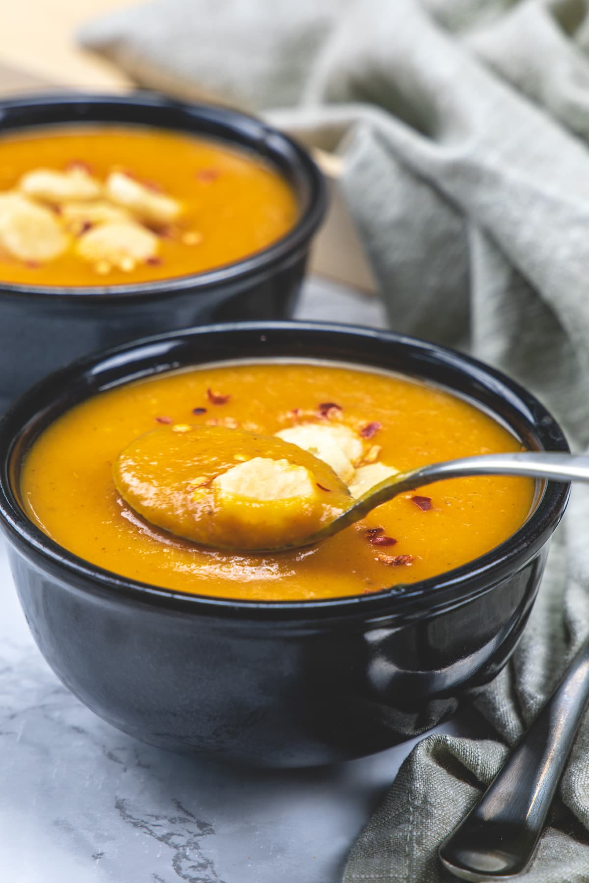a spoonful of carrot tomato soup is taken from the bowl and another bowl in the back.