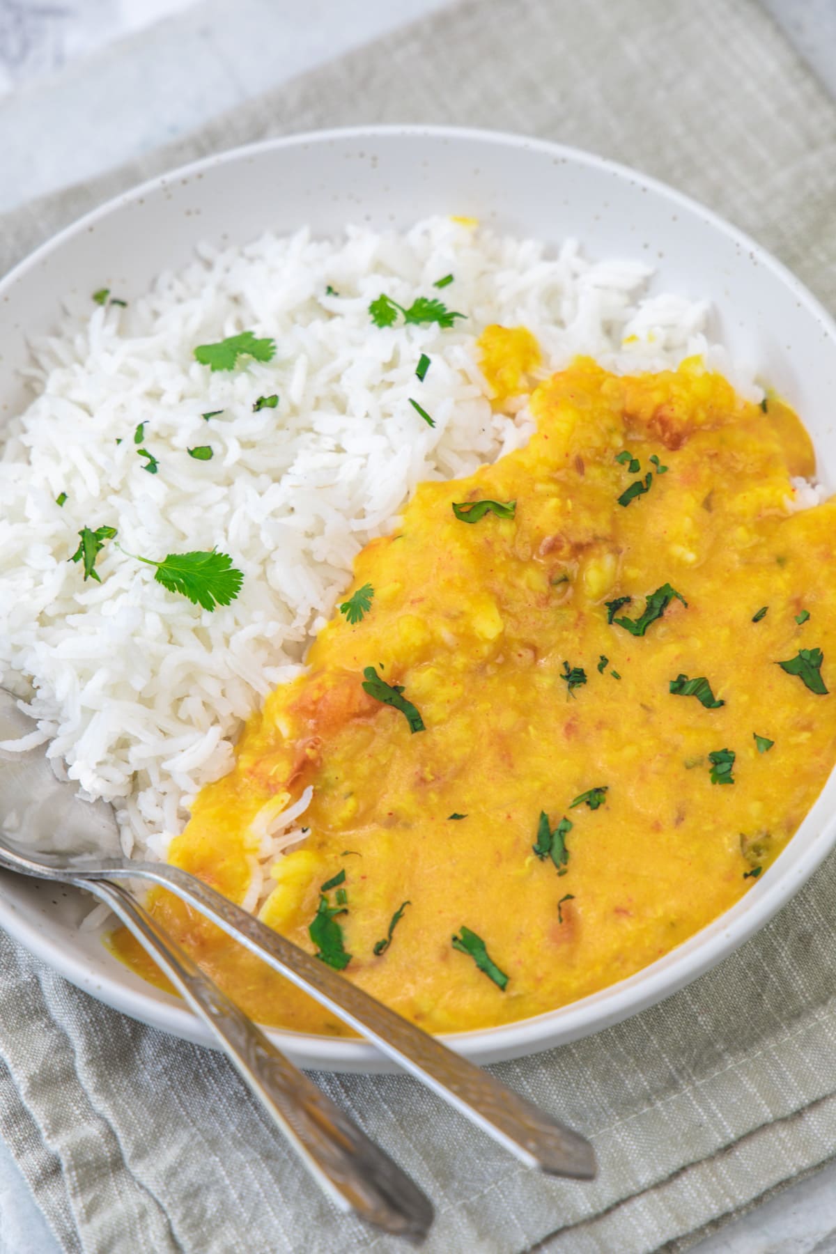 Moong dal served with rice in a plate garnished with cilantro and two spoond in a plate.