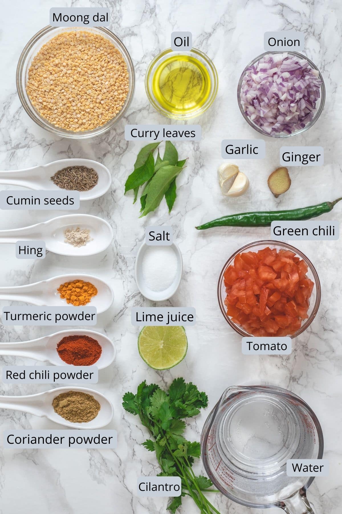 Ingredients used for moong dal with labels on marble background.