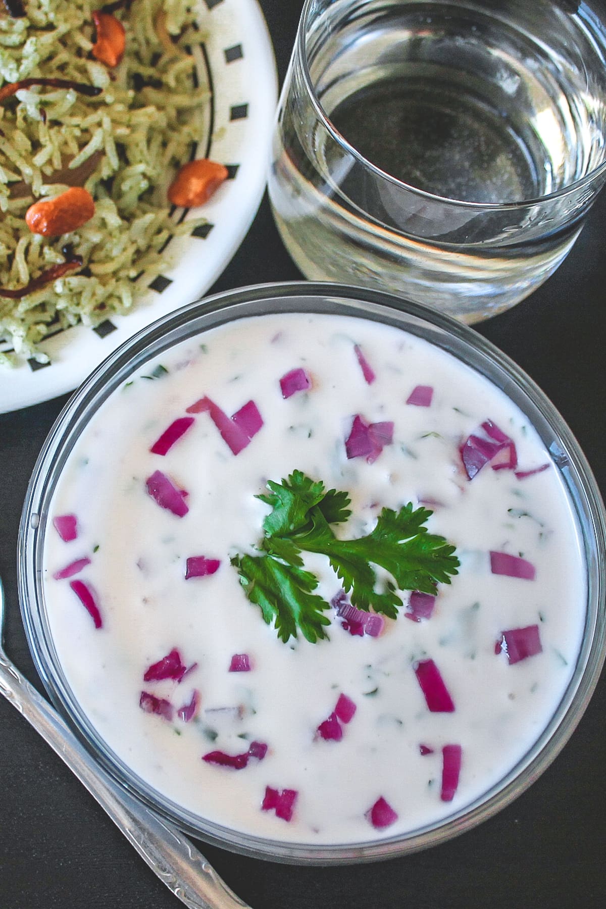 Onion raita garnished with cilantro and served with mint rice and a glass of water.