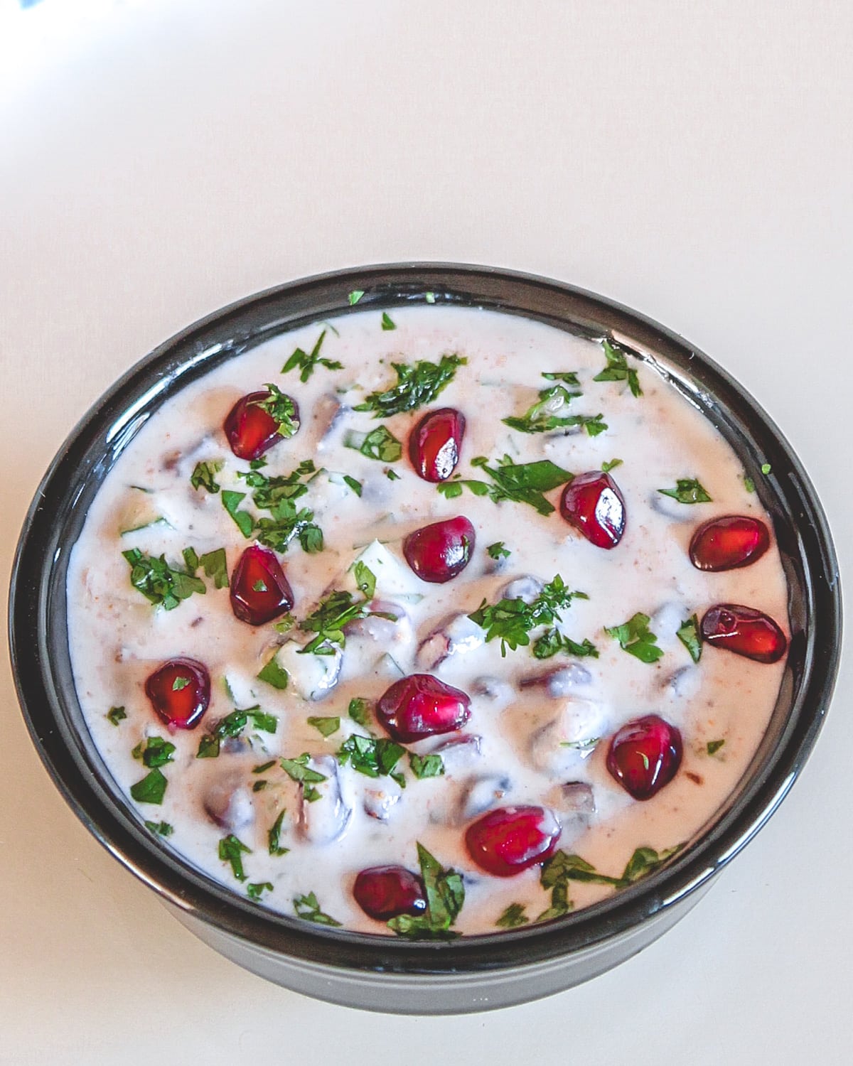 Pomegranate raita served in a black bowl garnish with cilantro and pomegranate arils.
