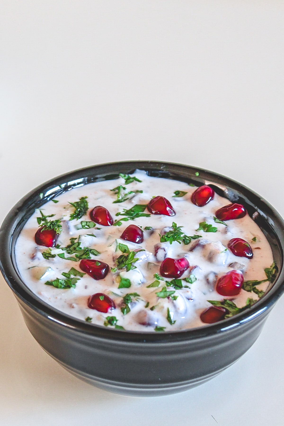 Pomegranate raita in a black bowl garnished with cilantro and arils.