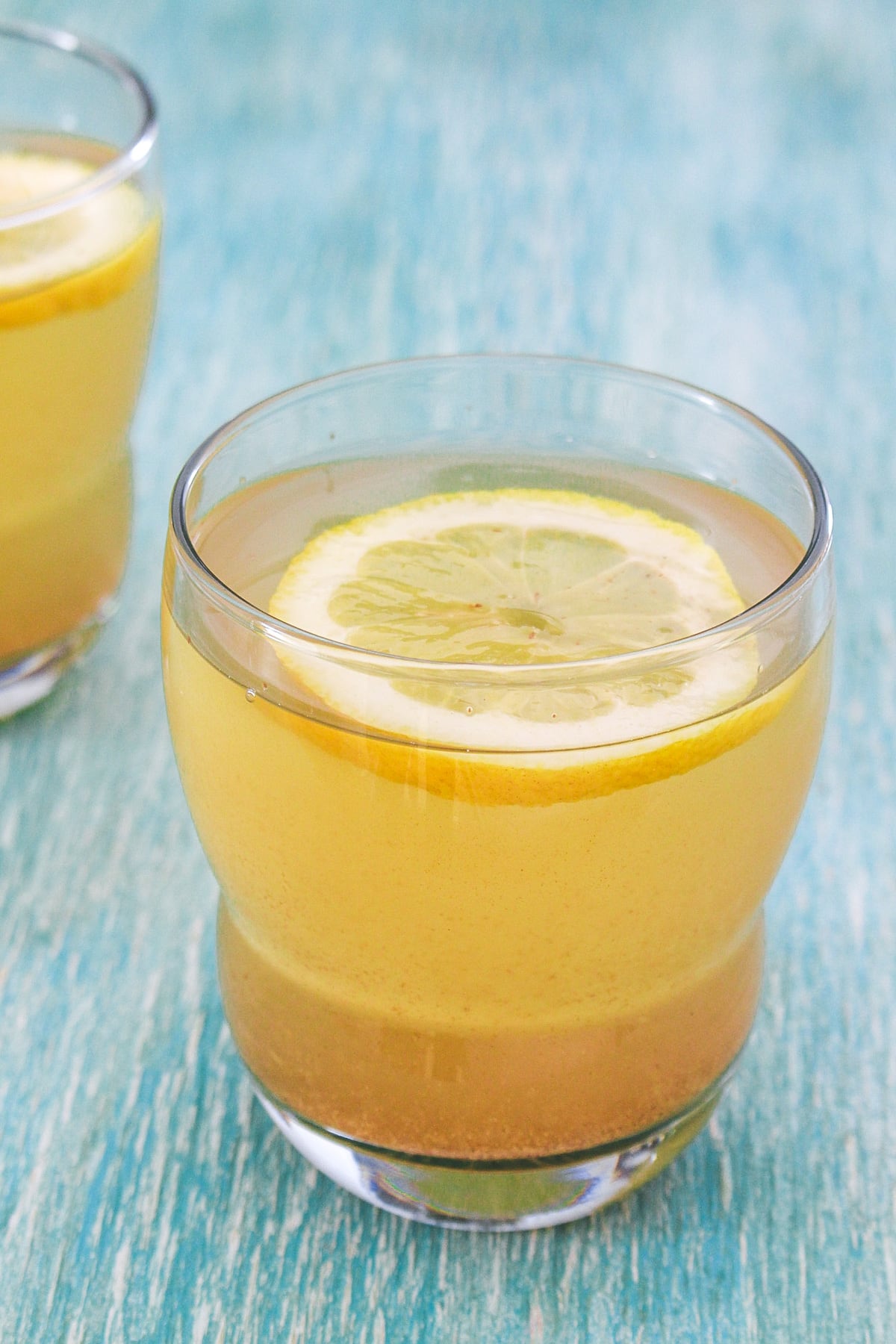 A glass of shikanji garnished with a lemon slice with another glass in the back side.