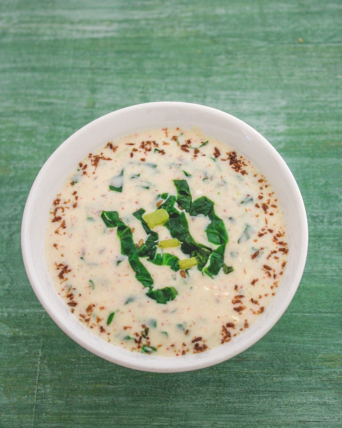 Spinach raita garnished with some cooked spinach and cumin powder.
