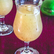 Aam panna served in a glass, anothe glass and a raw mango in the back.,