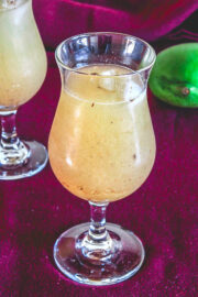 Aam panna served in a glass, anothe glass and a raw mango in the back.,