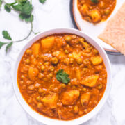 A bowl of aloo matar garnish with cilantro served with roti.