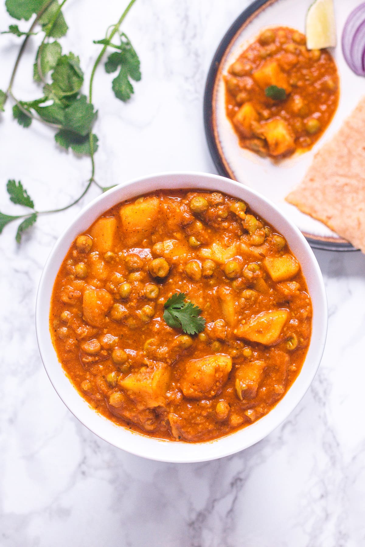 A bowl of aloo matar garnish with cilantro served with roti.