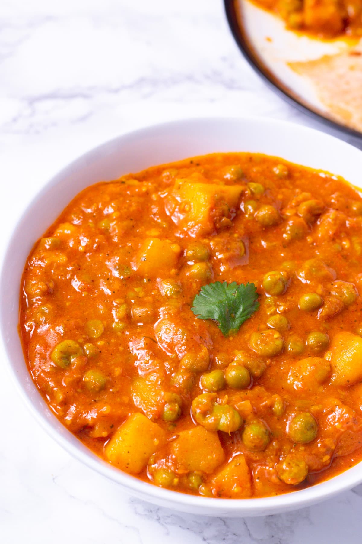 Aloo matar gravy served in a white bowl with a garnish of cilantro.