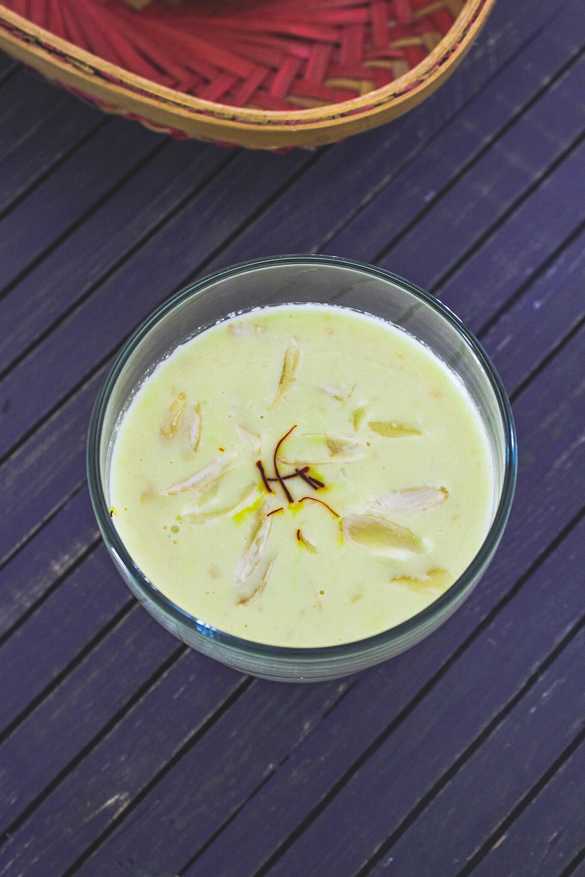 A glass of badam milk garnished with saffron strands and sliced almonds.