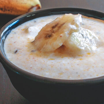 Banana raita served in a bowl with few banana slices on top.