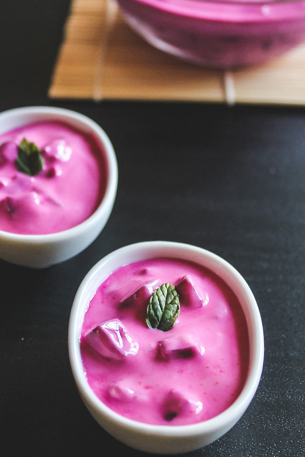 2 small bowls of beetroot raita garnished with mint leaves.