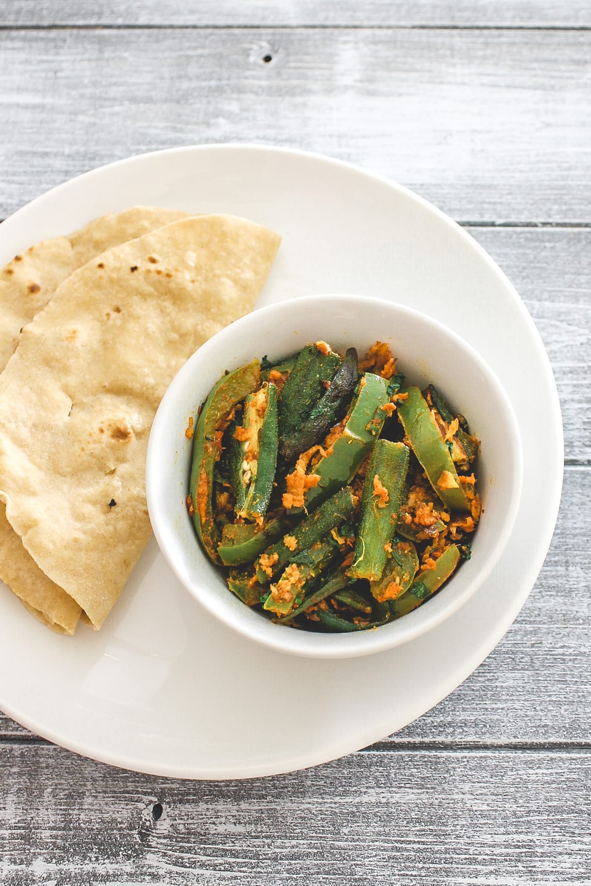 A plate with bhindi capsicum sabzi bowl and two roti.