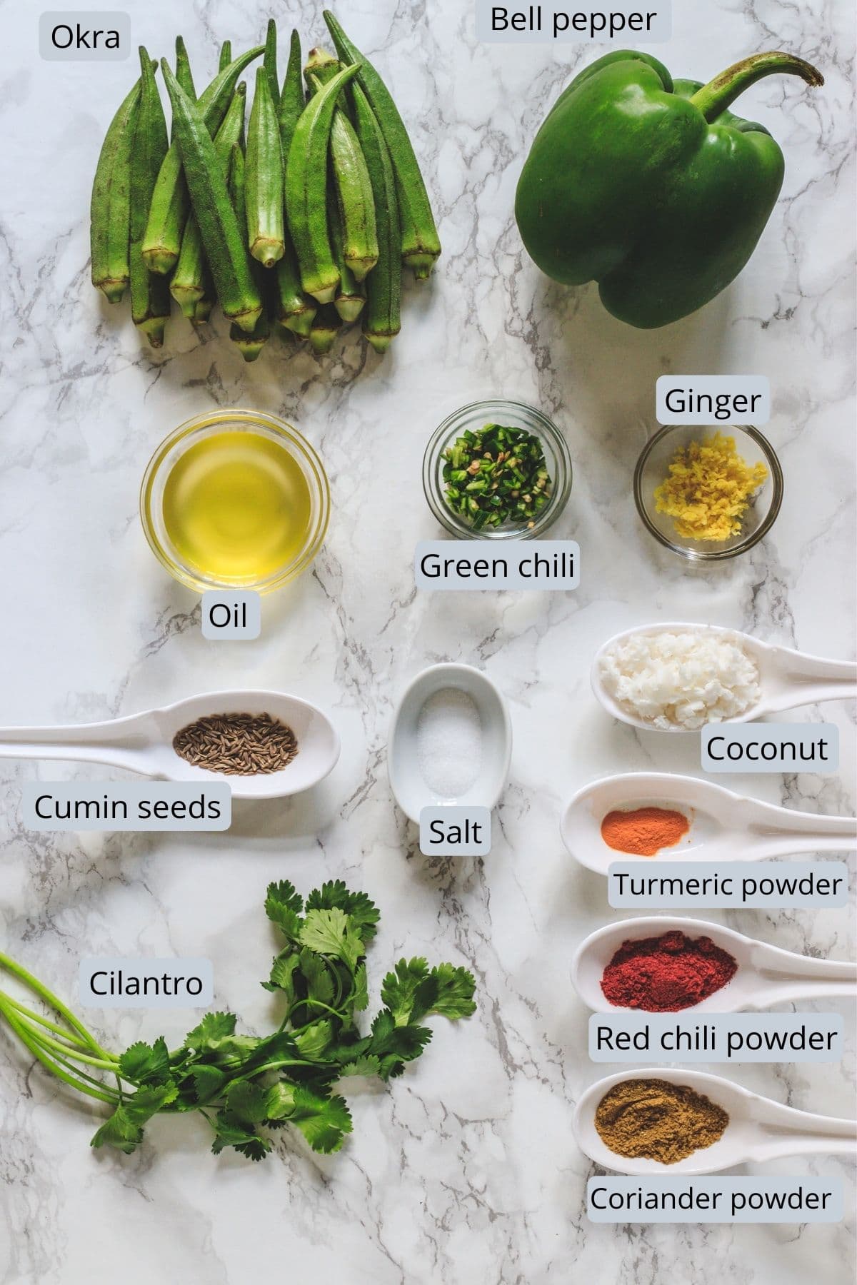 Ingredients for bhindi capsicum sabzi with labels on marble surface.