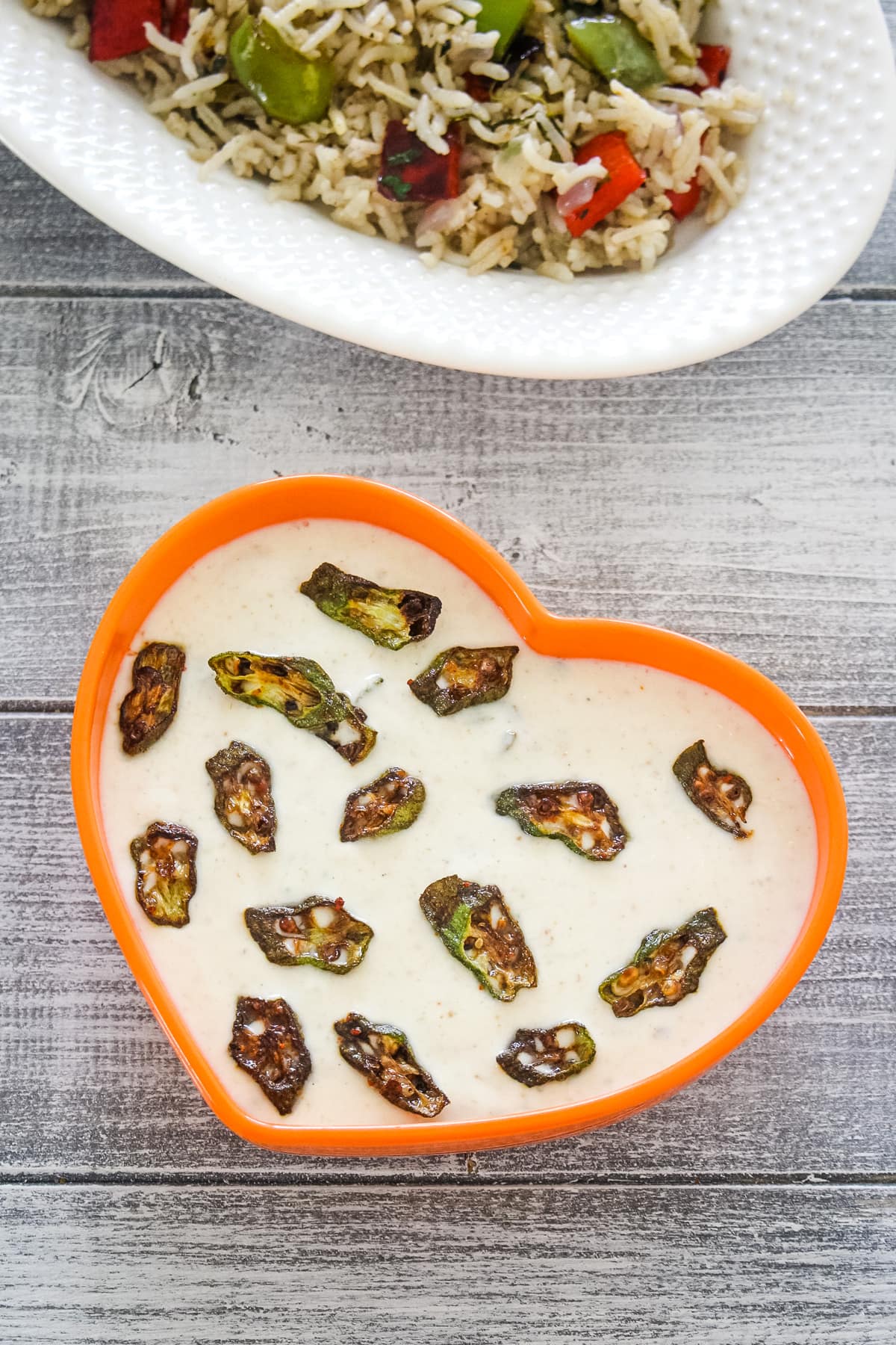 Okra raita in a heart shaped orange bowl with capsicum pulao.