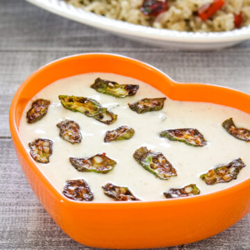 Bhindi raita in a orange bowl with pulao served on the side.