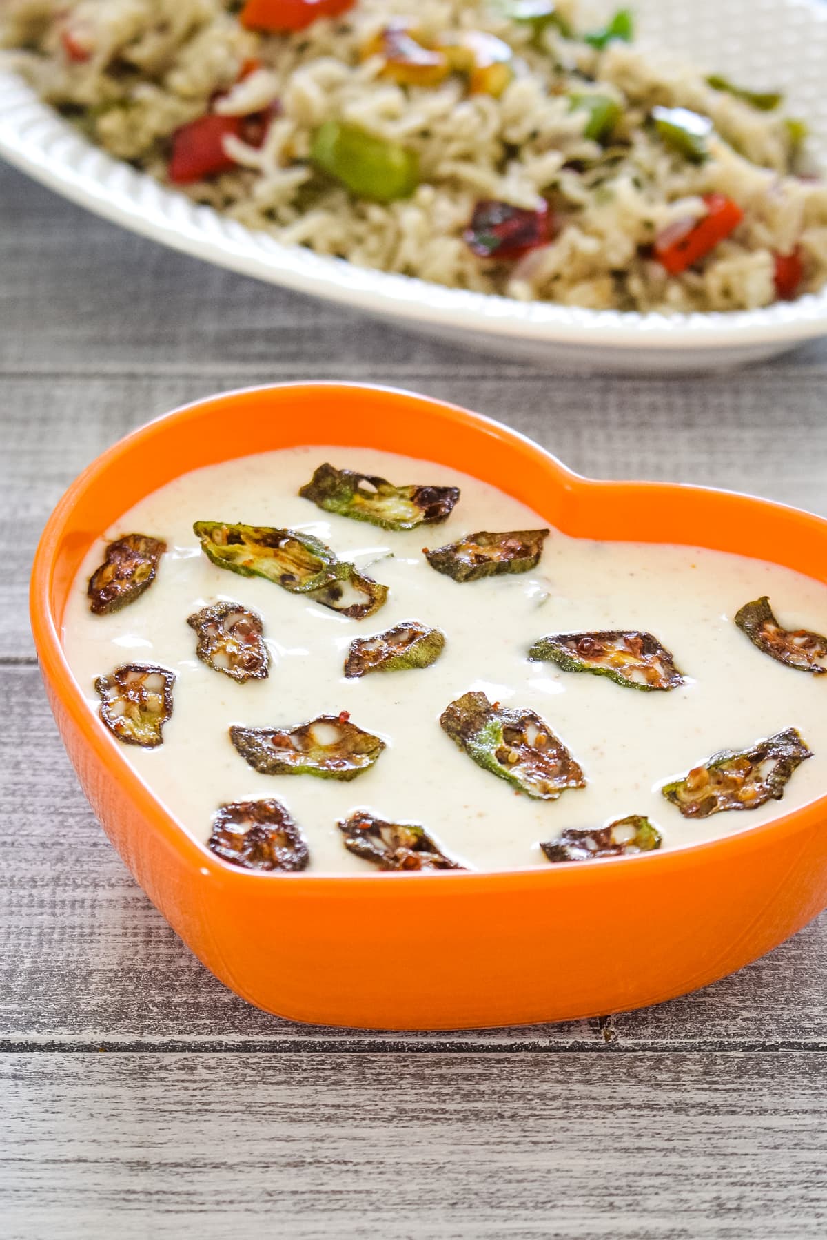 Bhindi raita in a orange bowl with pulao served on the side.