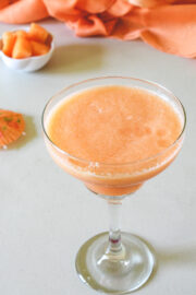 Cantaloupe juice in a glass with few cantaloupe cubes in the back.