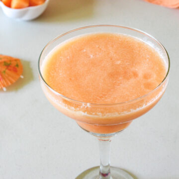 Cantaloupe juice in a glass with few cantaloupe cubes in the back.