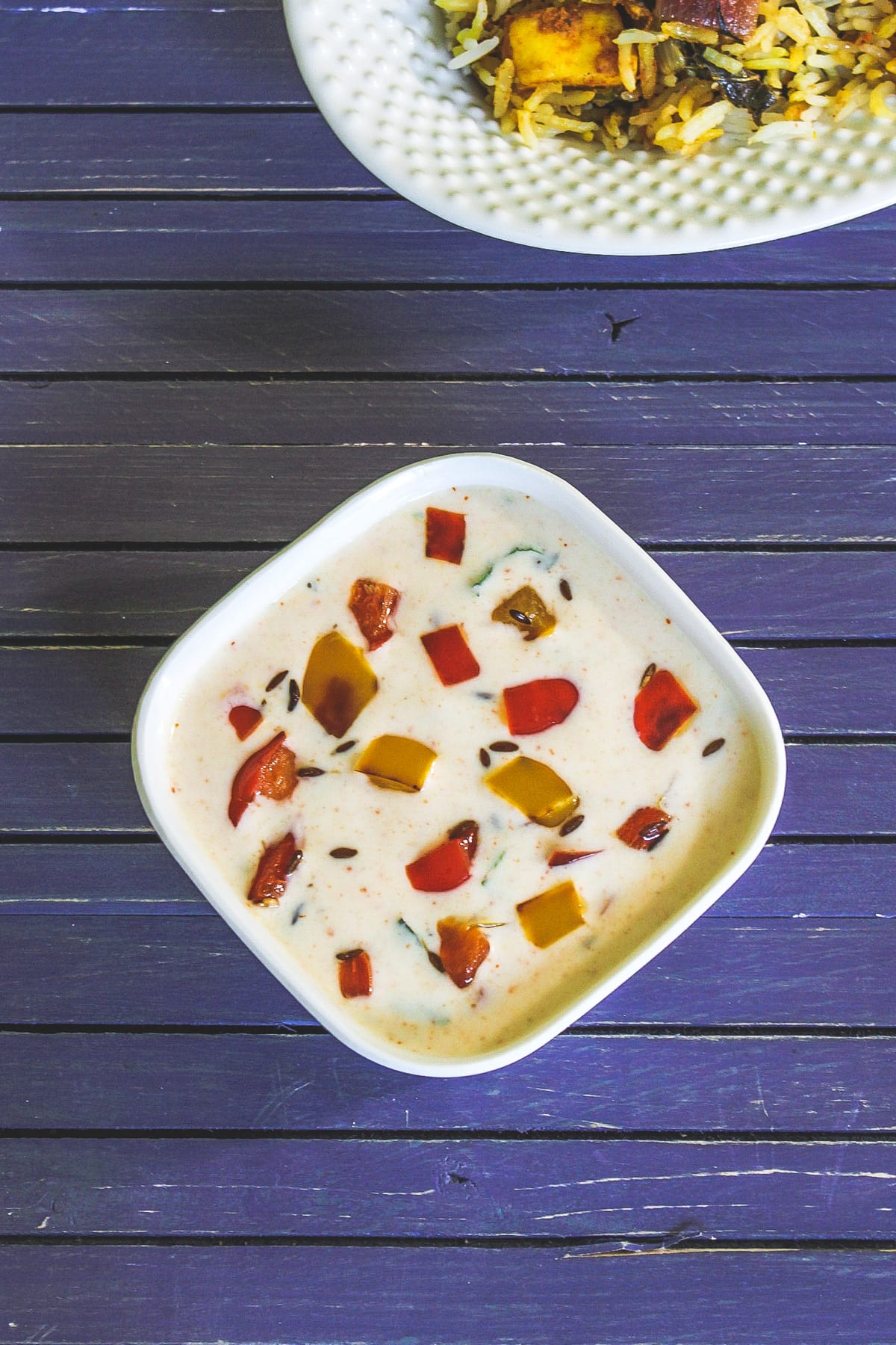 Capsicum raita in a bowl with biryani.
