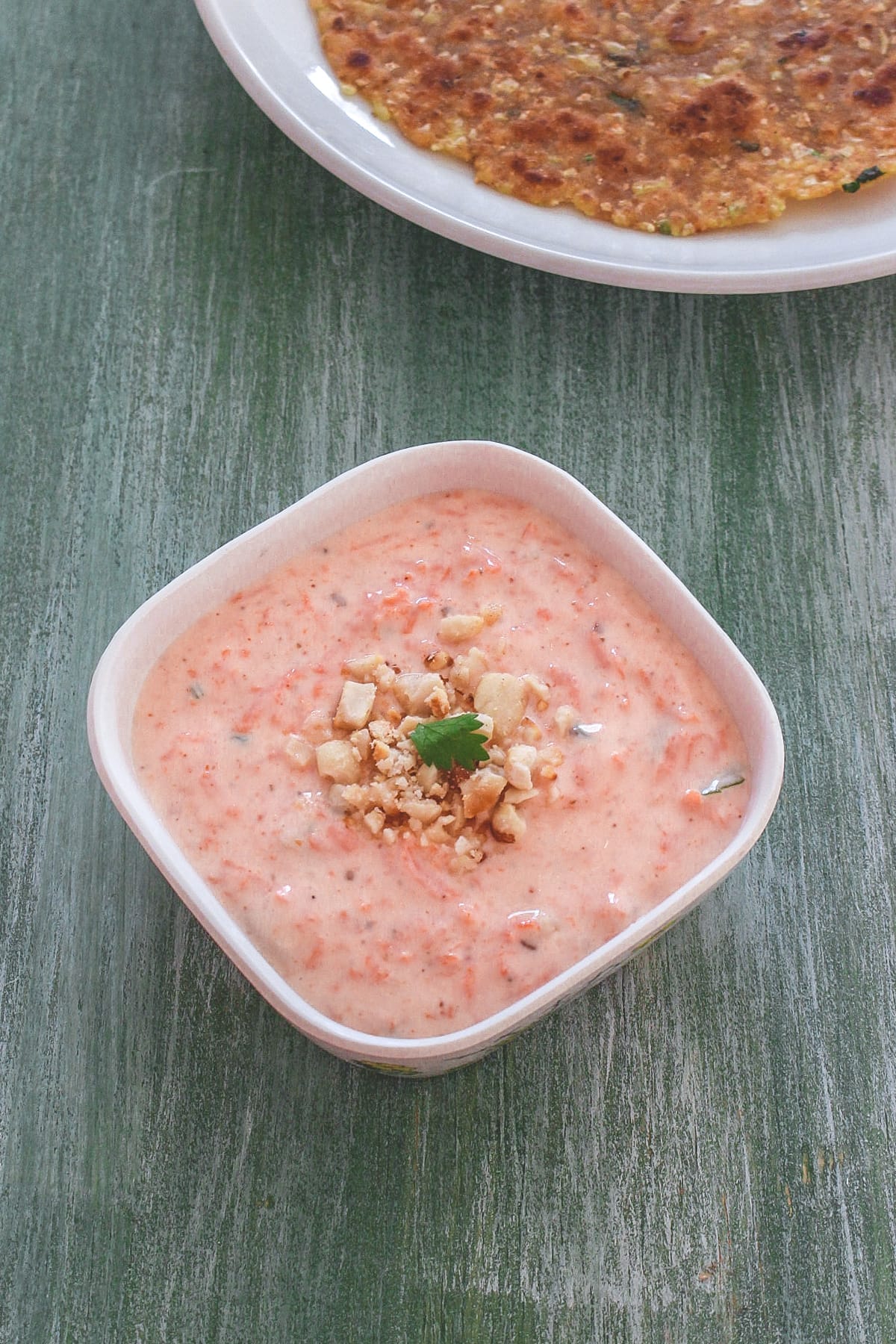 Carrot raita garnished with crushed peanuts and served with paratha.