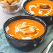 2 bowls of creamy Indian tomato soup topped with croutons and cream.