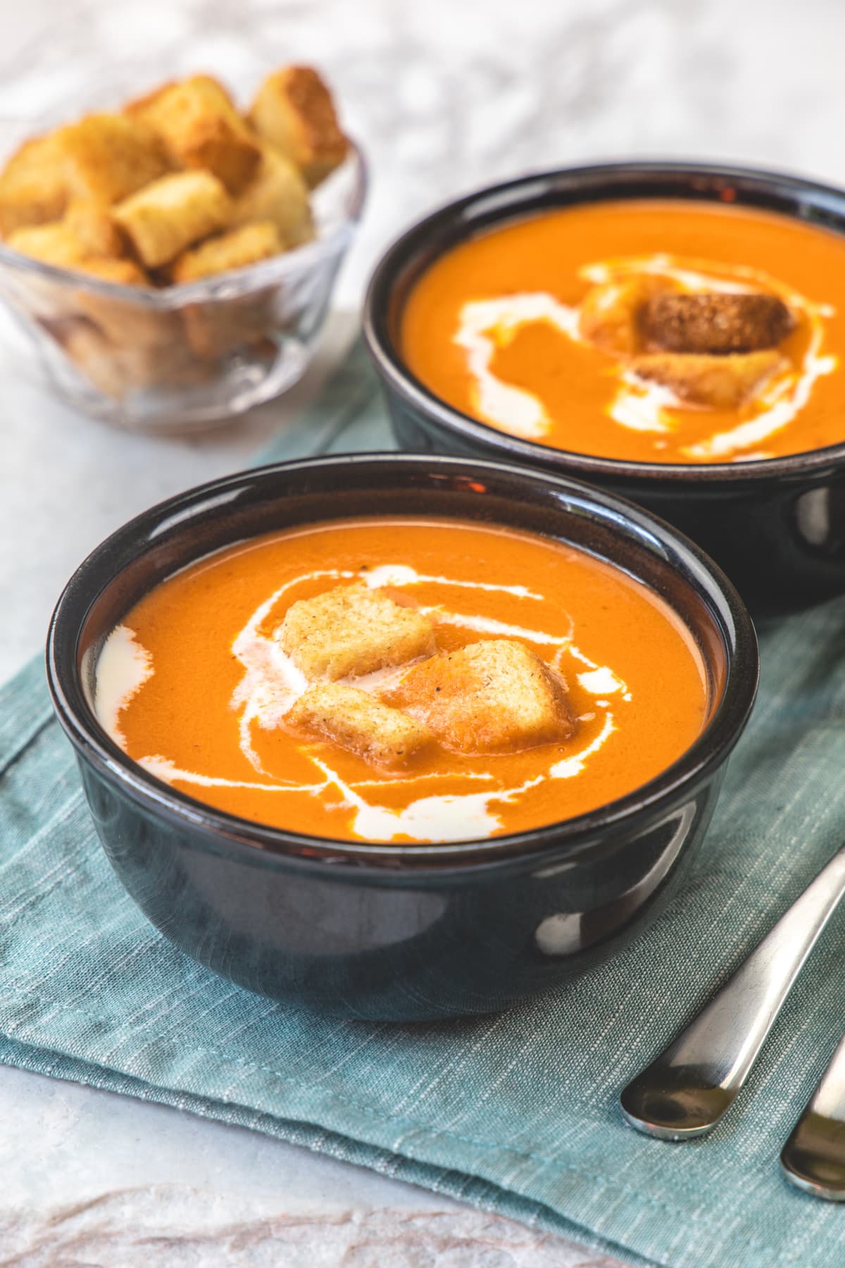 2 bowls of creamy Indian tomato soup topped with croutons and cream.
