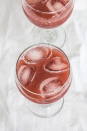 Grape juice served in a glass with ice cubes and other glass in the back.