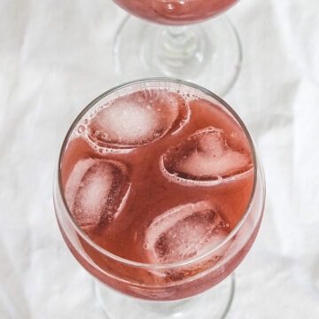 Grape juice served in a glass with ice cubes and other glass in the back.