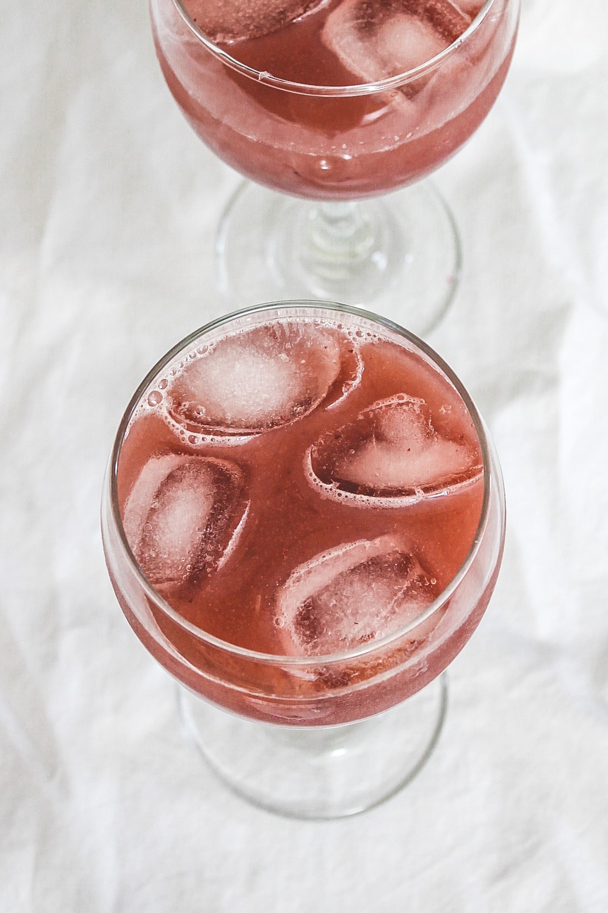 Grape juice served in a glass with ice cubes and other glass in the back.