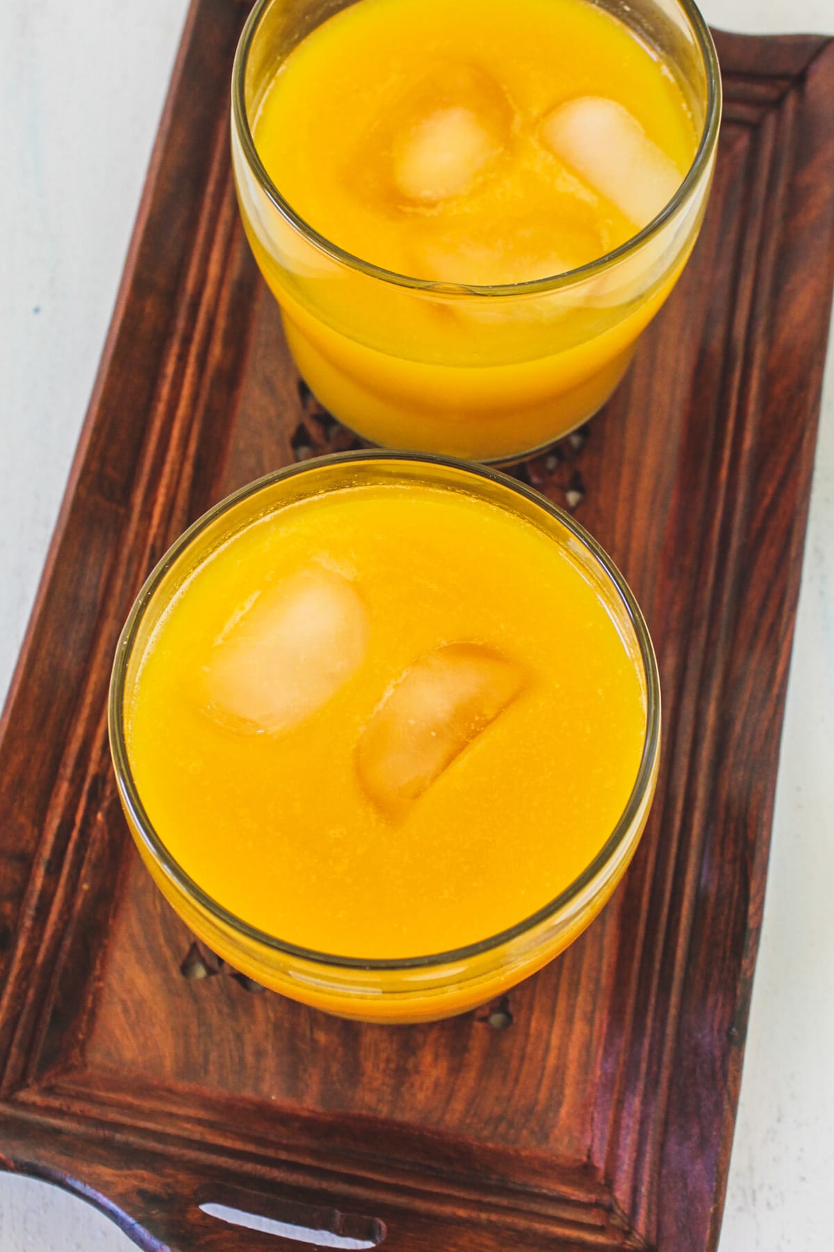 Mango juice with ice cubes in 2 glasses in a tray.