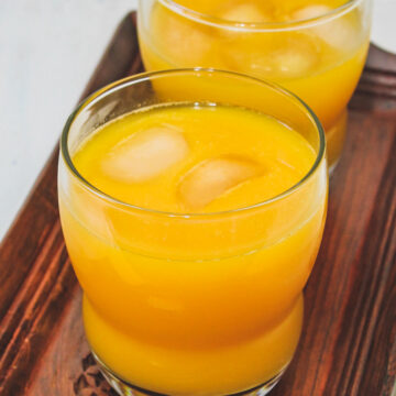 2 glass of mango juice in a wooden tray.