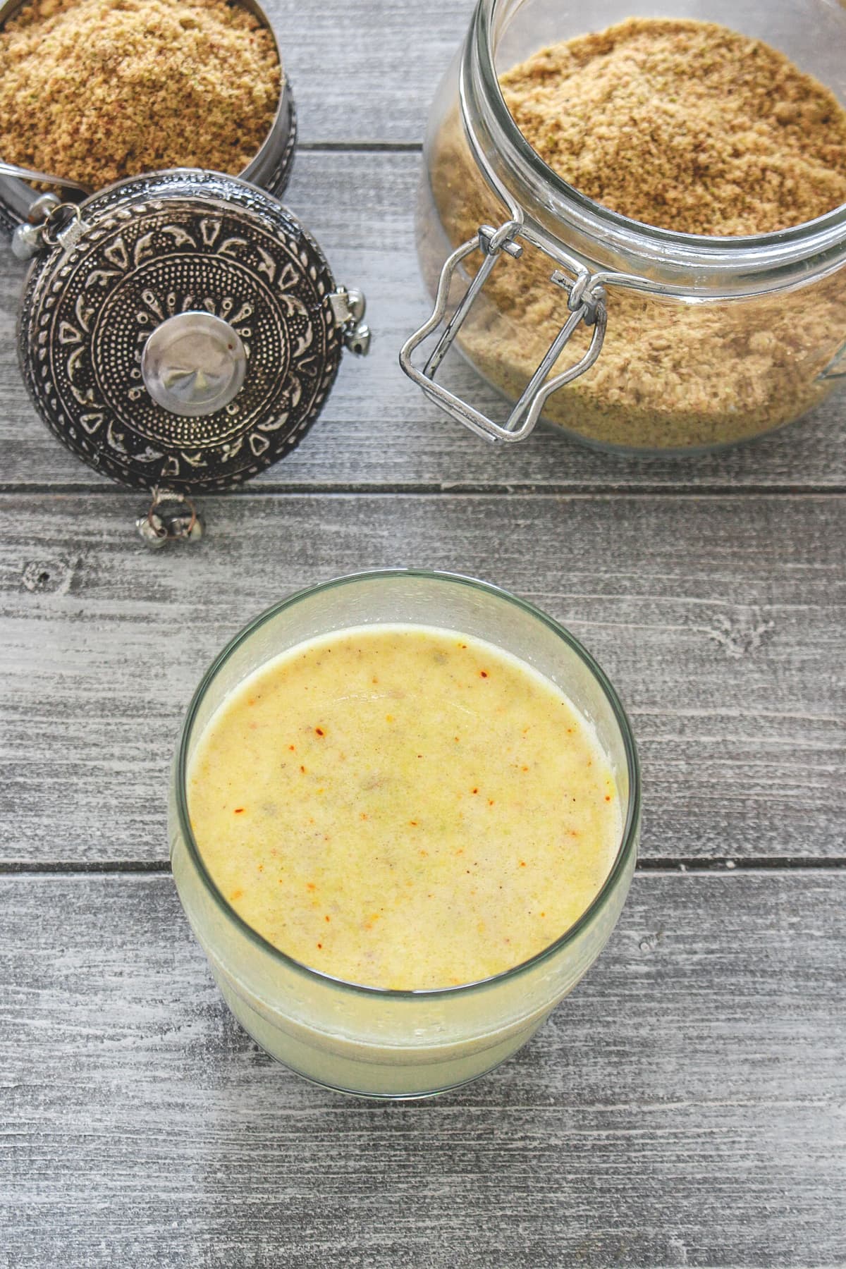 Masala doodh in a glass with milk masala powder bowl and container in the back.