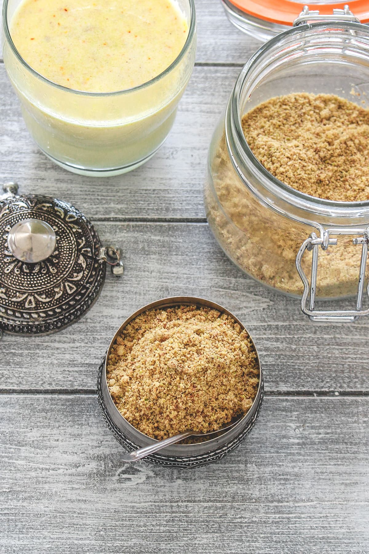 Milk masala powder bowl with lid, a container and a glass of masala doodh.