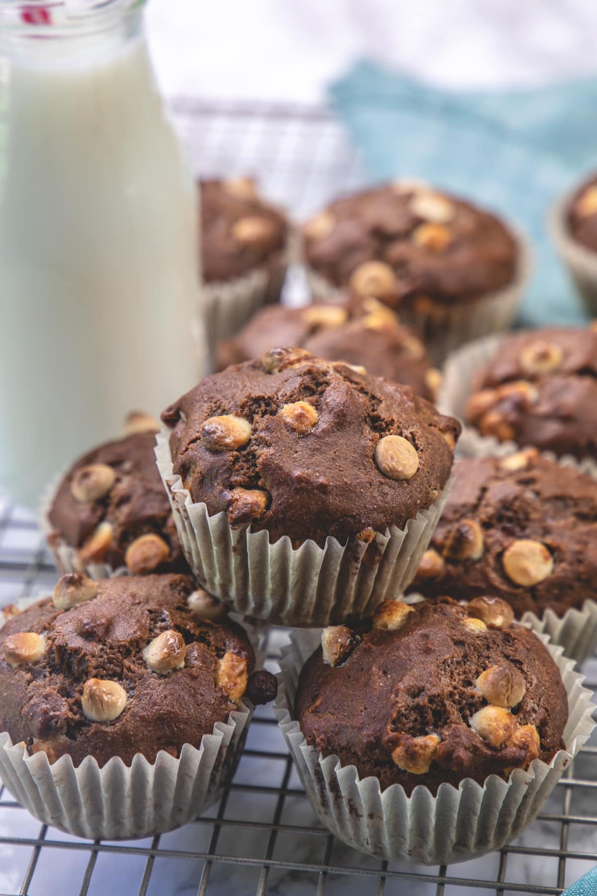 Stacked mocha muffins on a cooling rach with bottle of milk in the back.