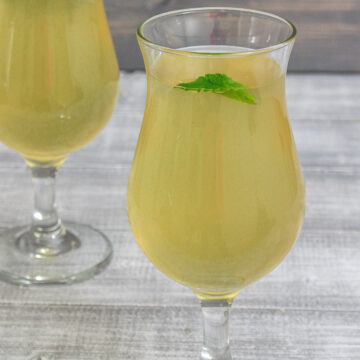 2 glasses of nimbu pani garnished with mint leaves.