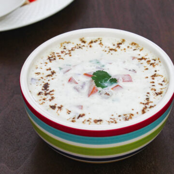 Onion tomato raita in a bowl garnish with cumin powder and cilantro.