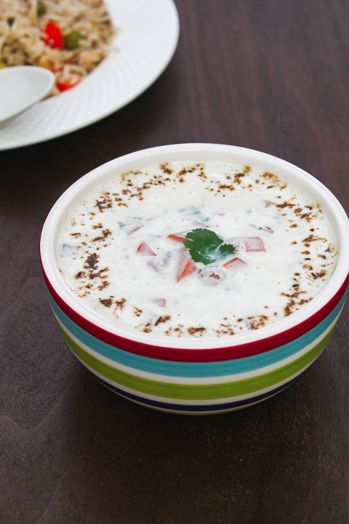 Onion tomato raita in a bowl garnish with cumin powder and cilantro.