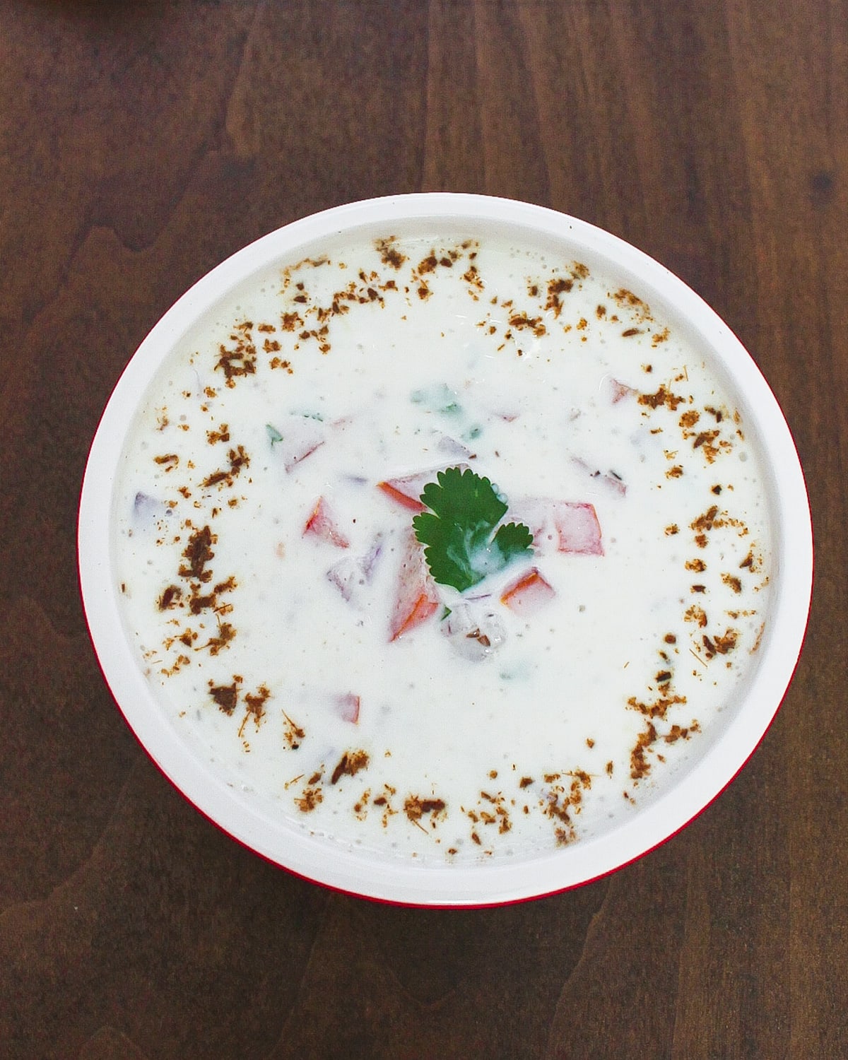 Onion tomato raita served in a bowl that is garnished with cilantro and spice powder.