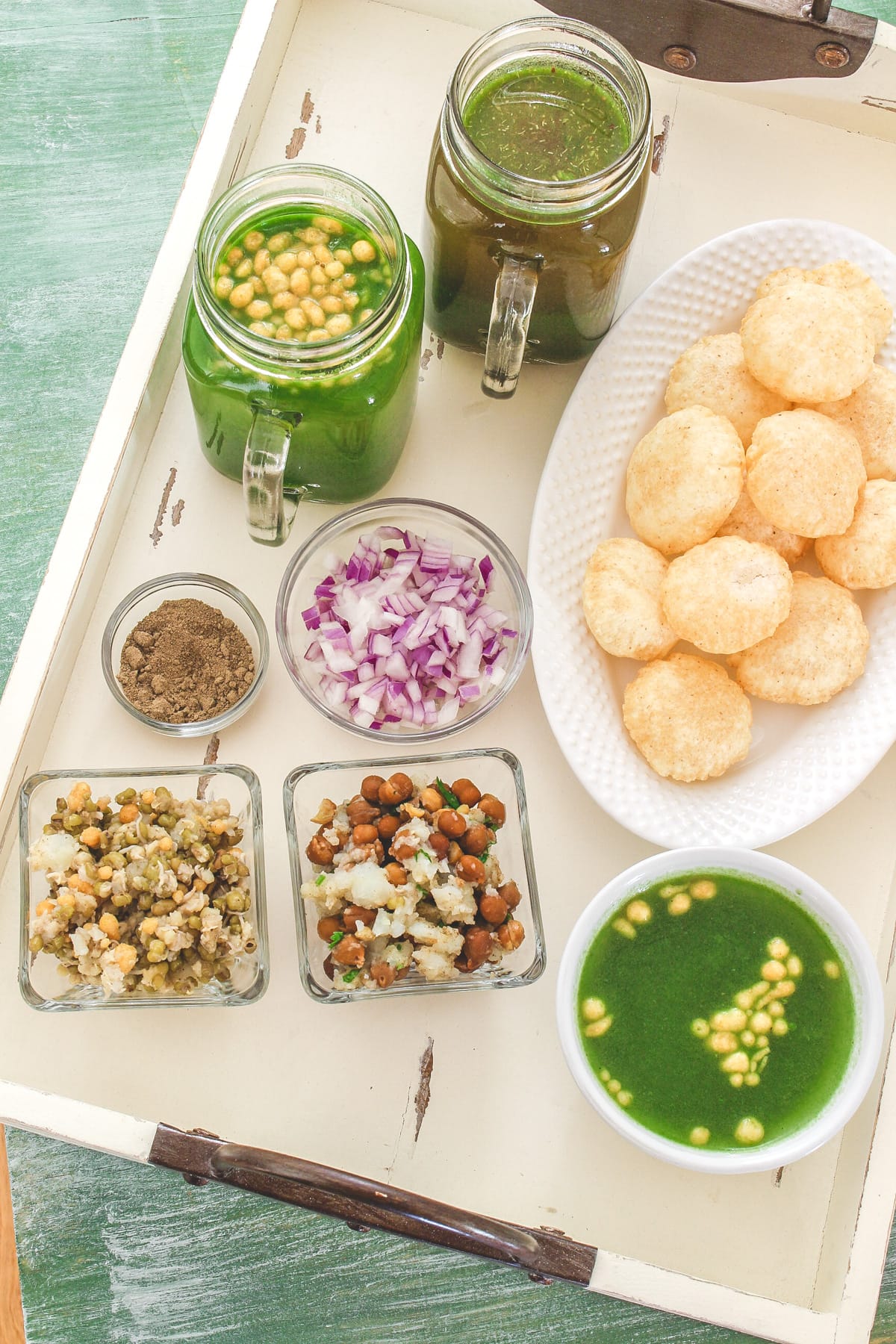 2 bowls of stuffing, 2 mugs and a bowl of water, with puri, onion and masala.