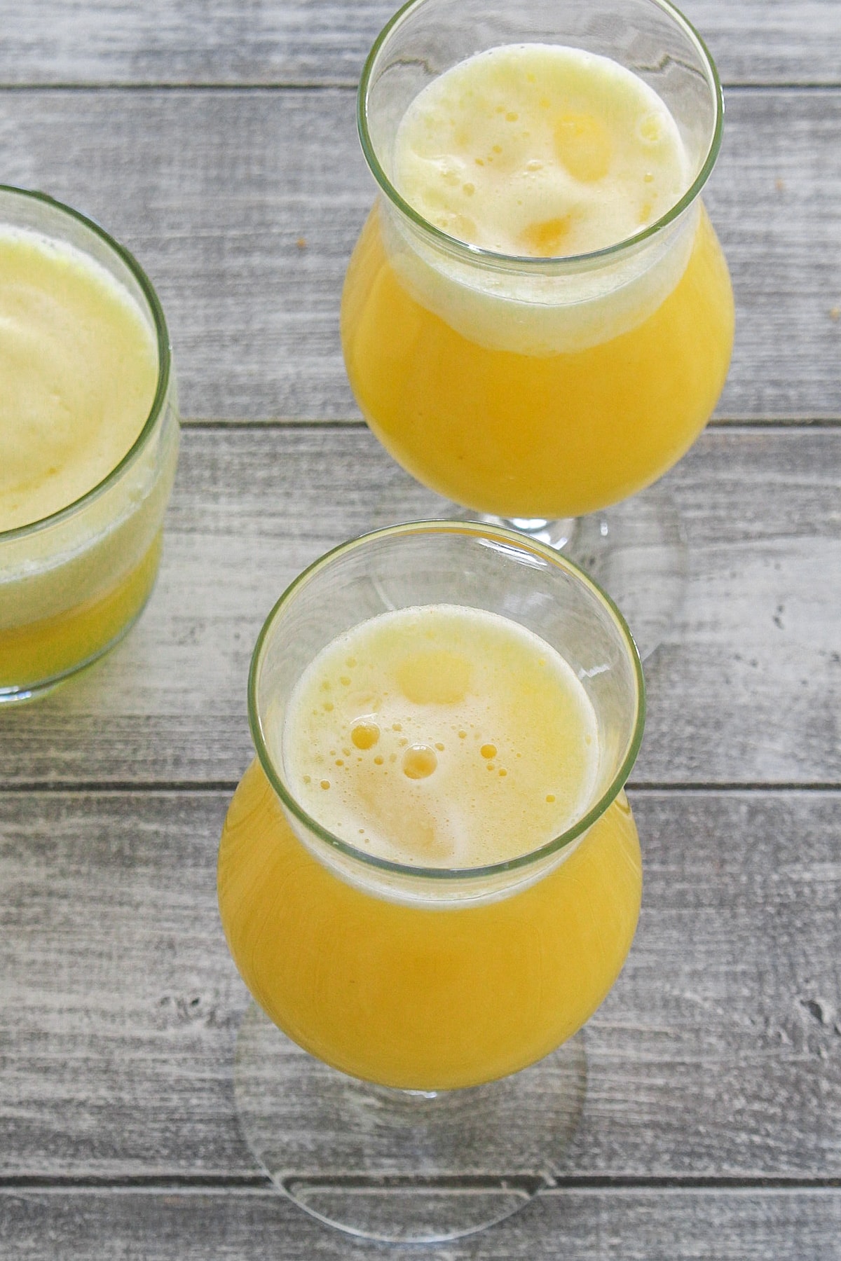 3 glasses of pineapple juice on a white board.