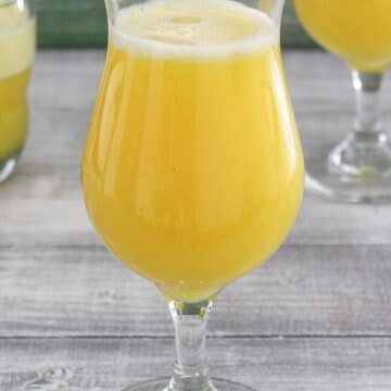 A glass of pineapple juice with 2 glasses in the back.