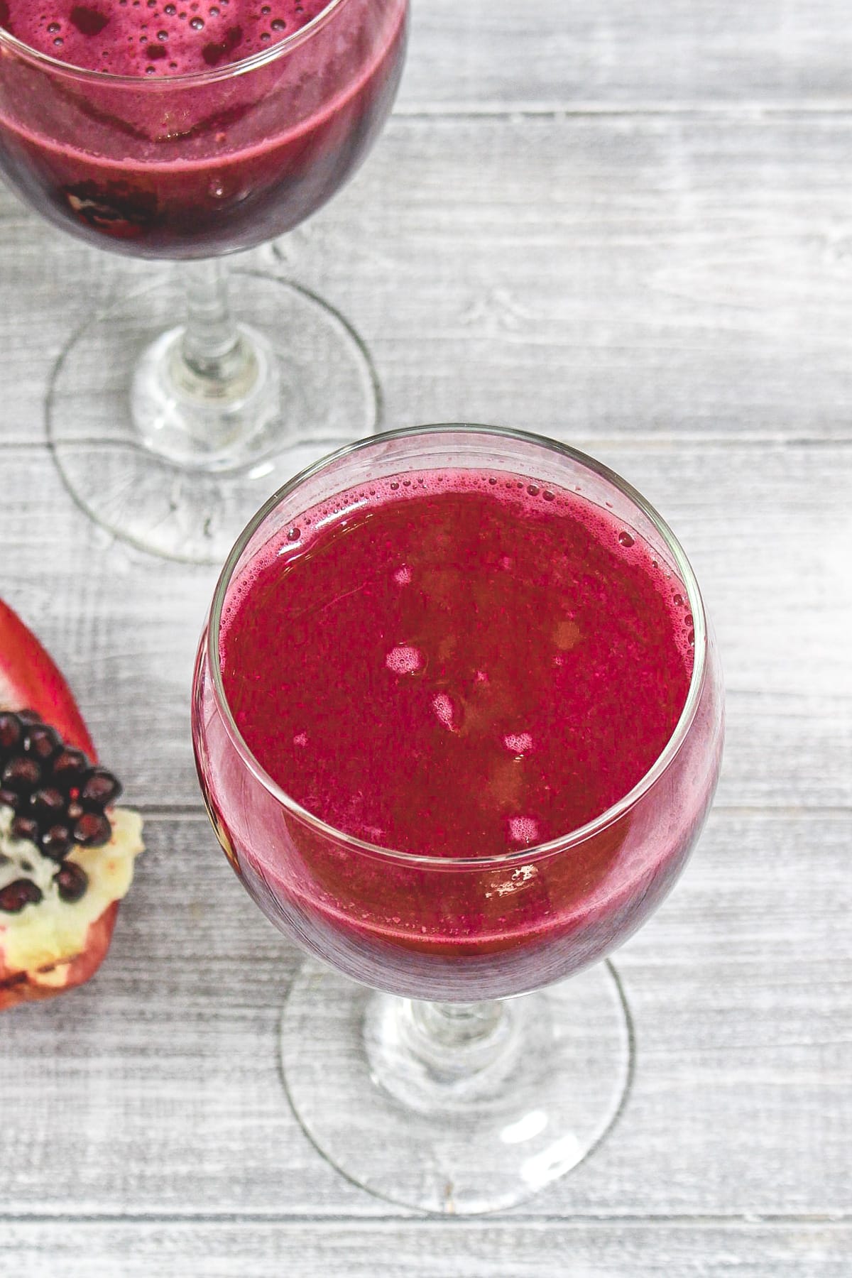 2 glasses of pomegranate juice with a pomegranate wedge on side.